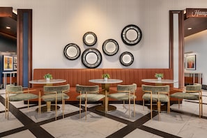Um interior moderno com área de estar com mesas redondas e cadeiras estofadas, parede com espelhos circulares e um aviso que diz 'Hamp'.