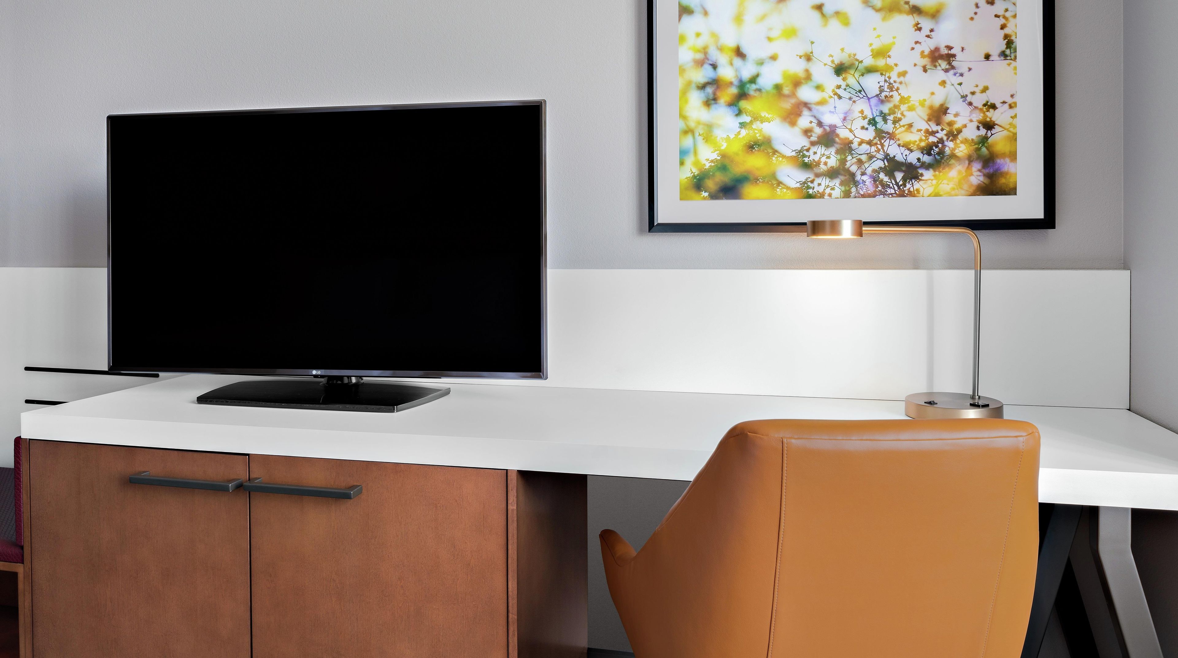A modern office space with a flat-screen TV, a desk, a chair, and a framed picture on the wall.