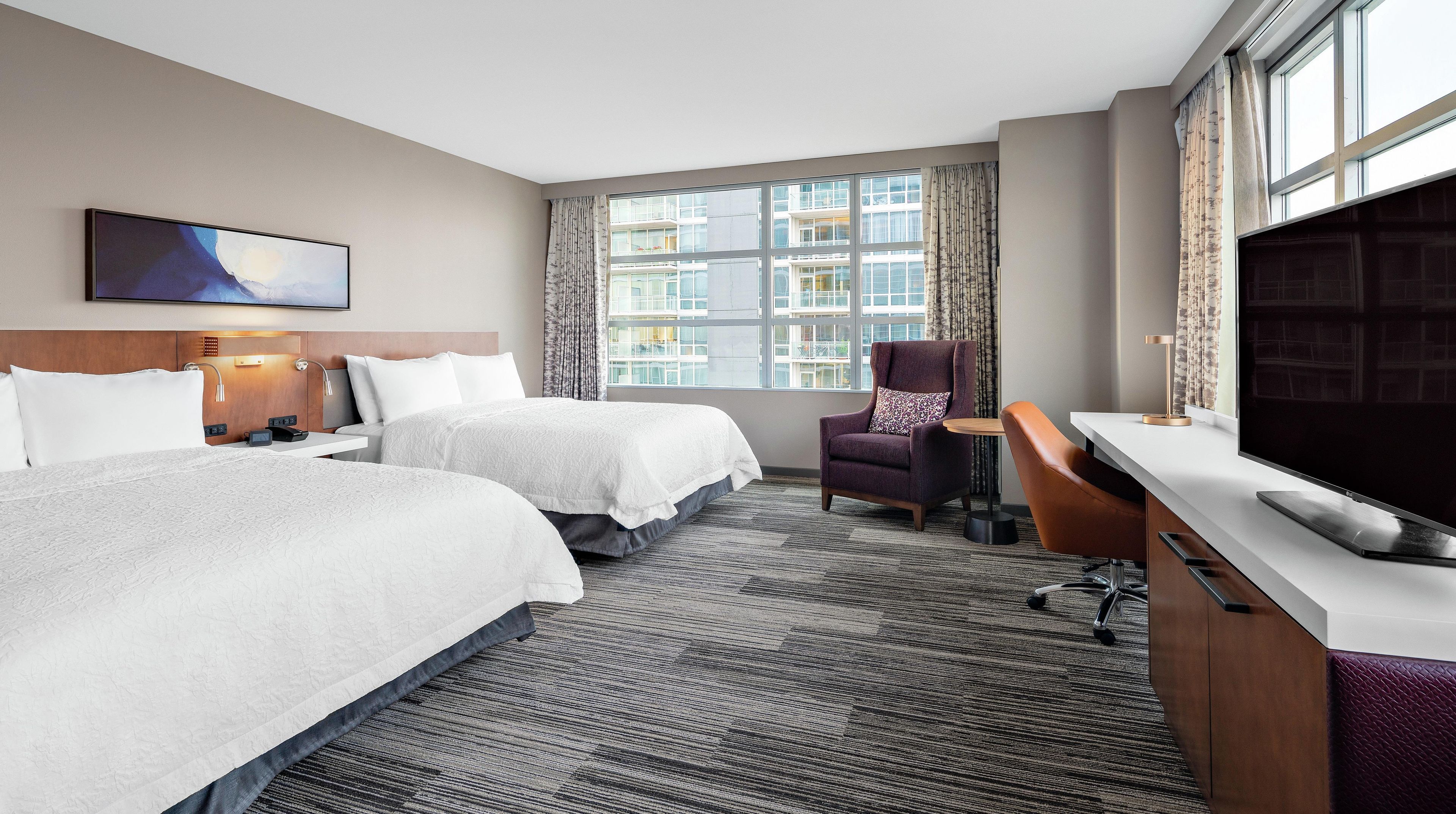 A hotel room with two beds, a TV, a desk, and a chair.