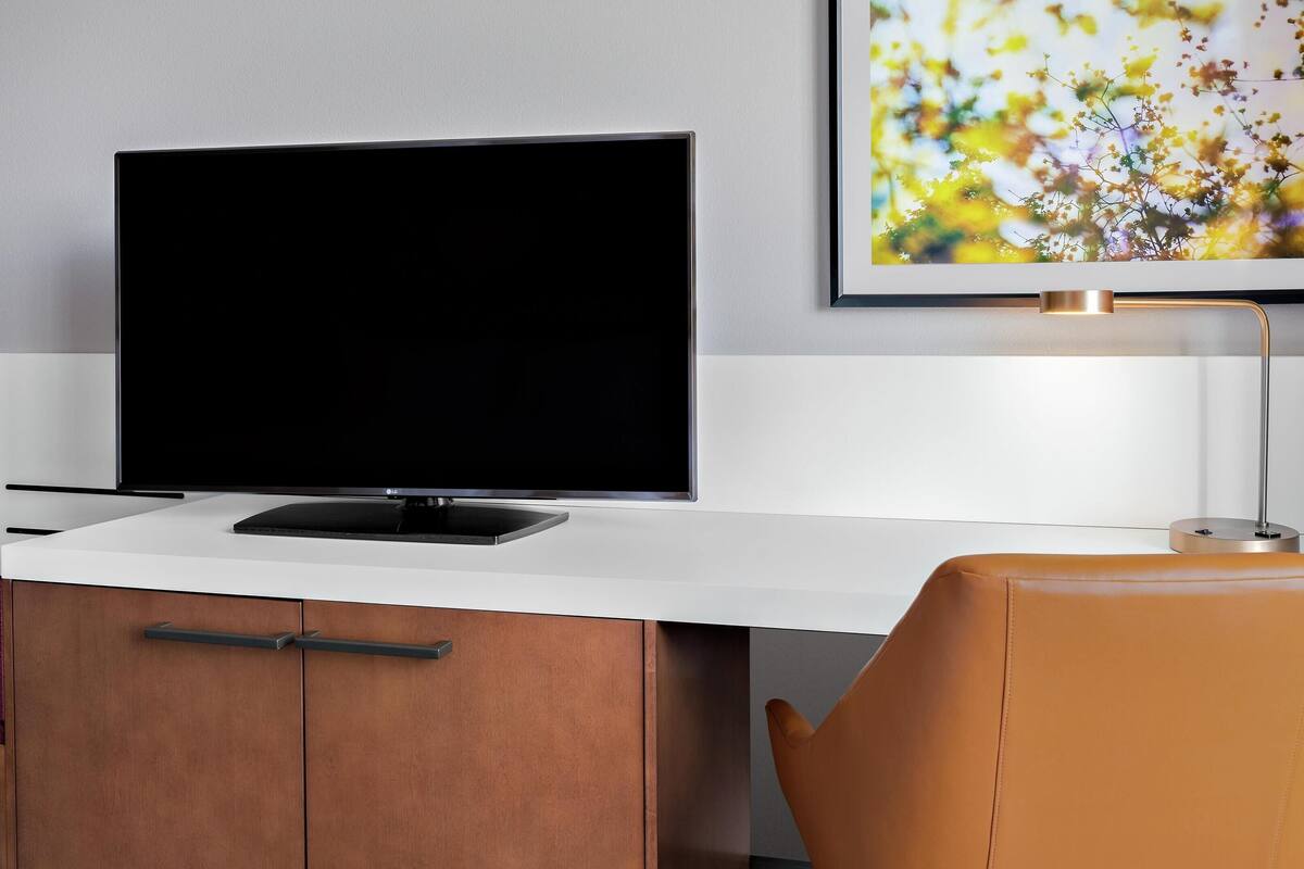 Un espace de bureau moderne équipé d’un téléviseur à écran plat, d’un bureau, d’une chaise et d’un tableau encadré au mur.