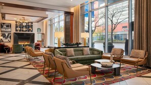 A modern lobby with a fireplace, comfortable seating, and large windows offering a view of the outside. - Hilton Garden Inn Chicago McCormick Place (Chicago)