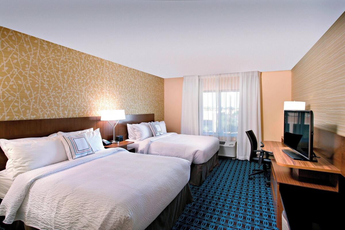 A hotel room with two beds, a desk with a computer, a TV, and a window with curtains.