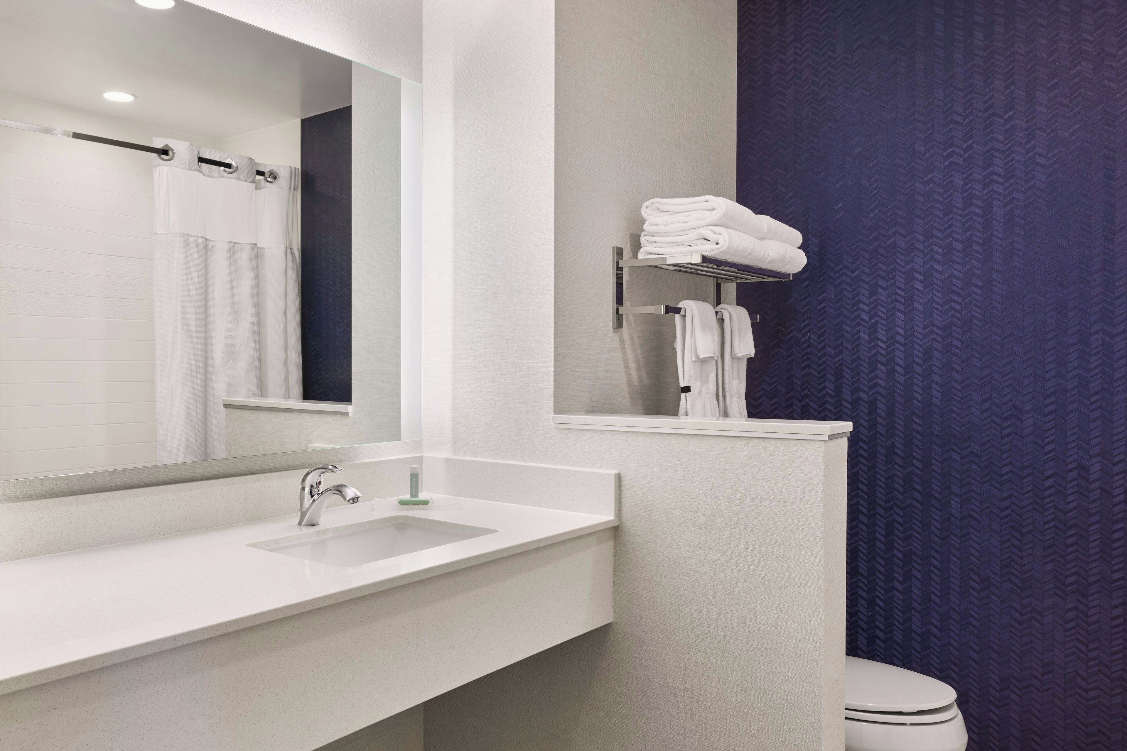 A modern bathroom with a white sink, a mirror, a towel rack, and a toilet.