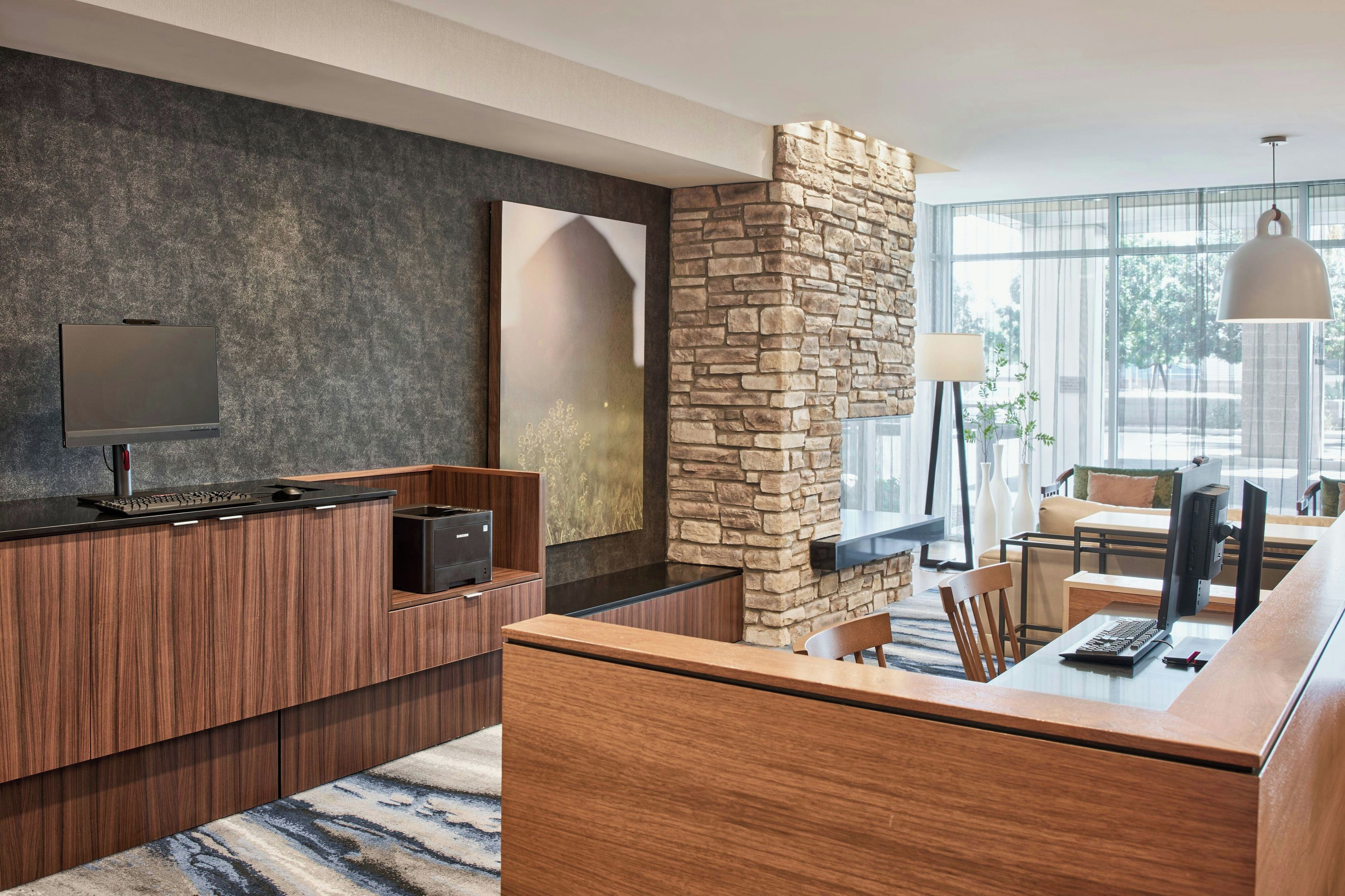 A modern hotel lobby with a reception desk, a stone accent wall, and a large window offering a view of the outdoors.