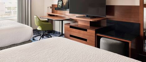 A hotel room with a bed, a desk with a television, a chair, and a window with curtains.