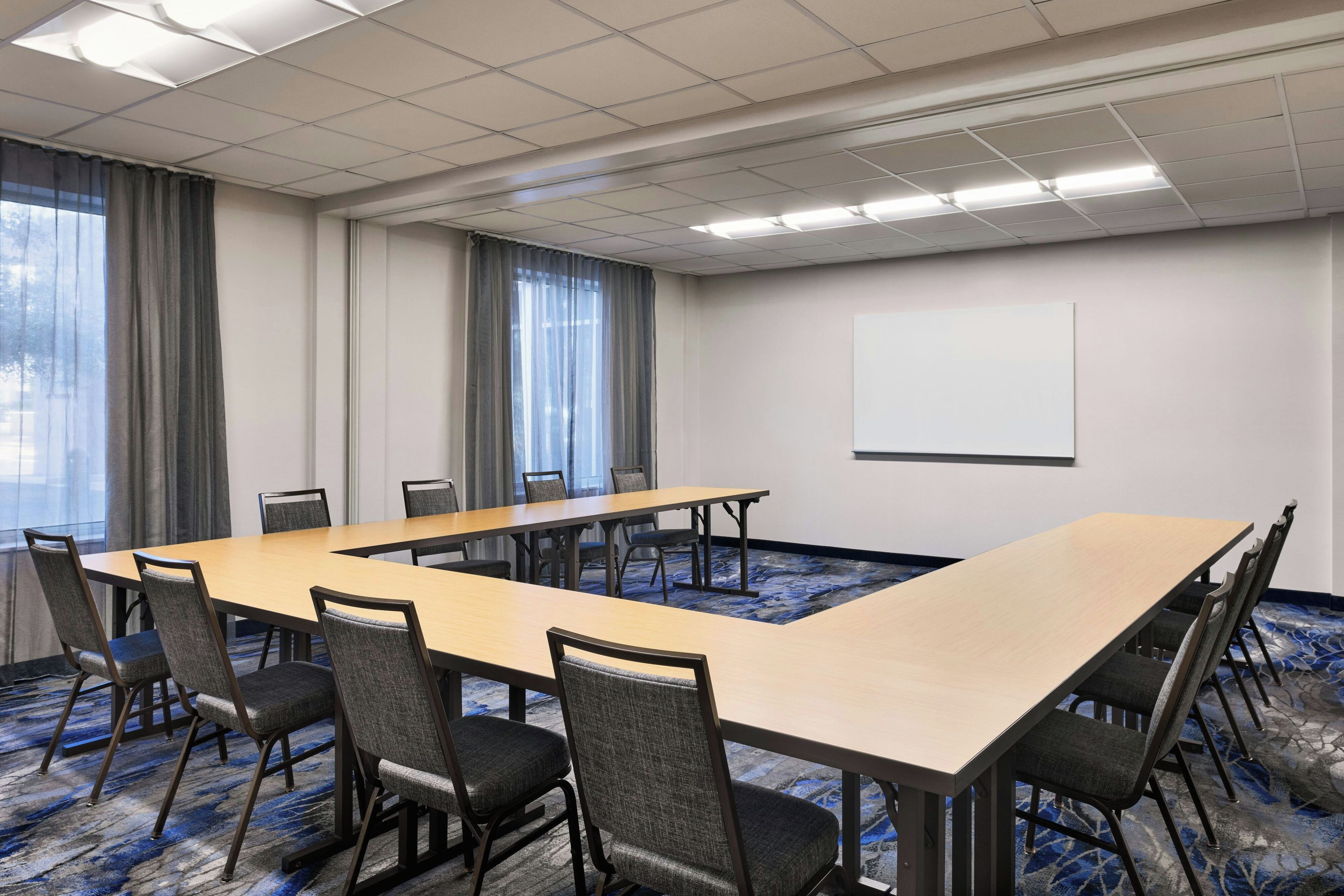 A conference room with a long table, chairs, a projector screen, and large windows with curtains.