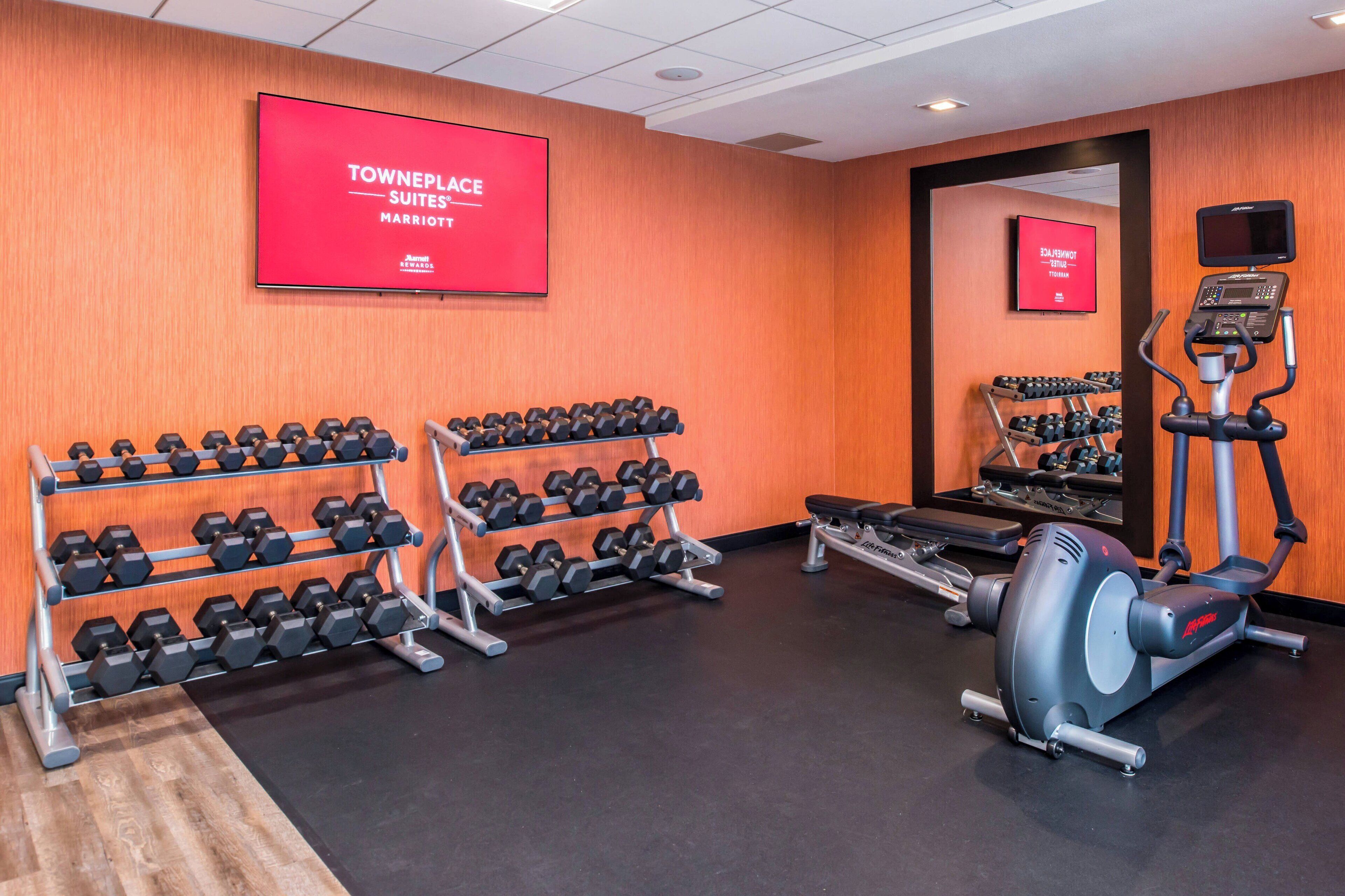 A gym with dumbbells, a treadmill, and a mirrored wall.
