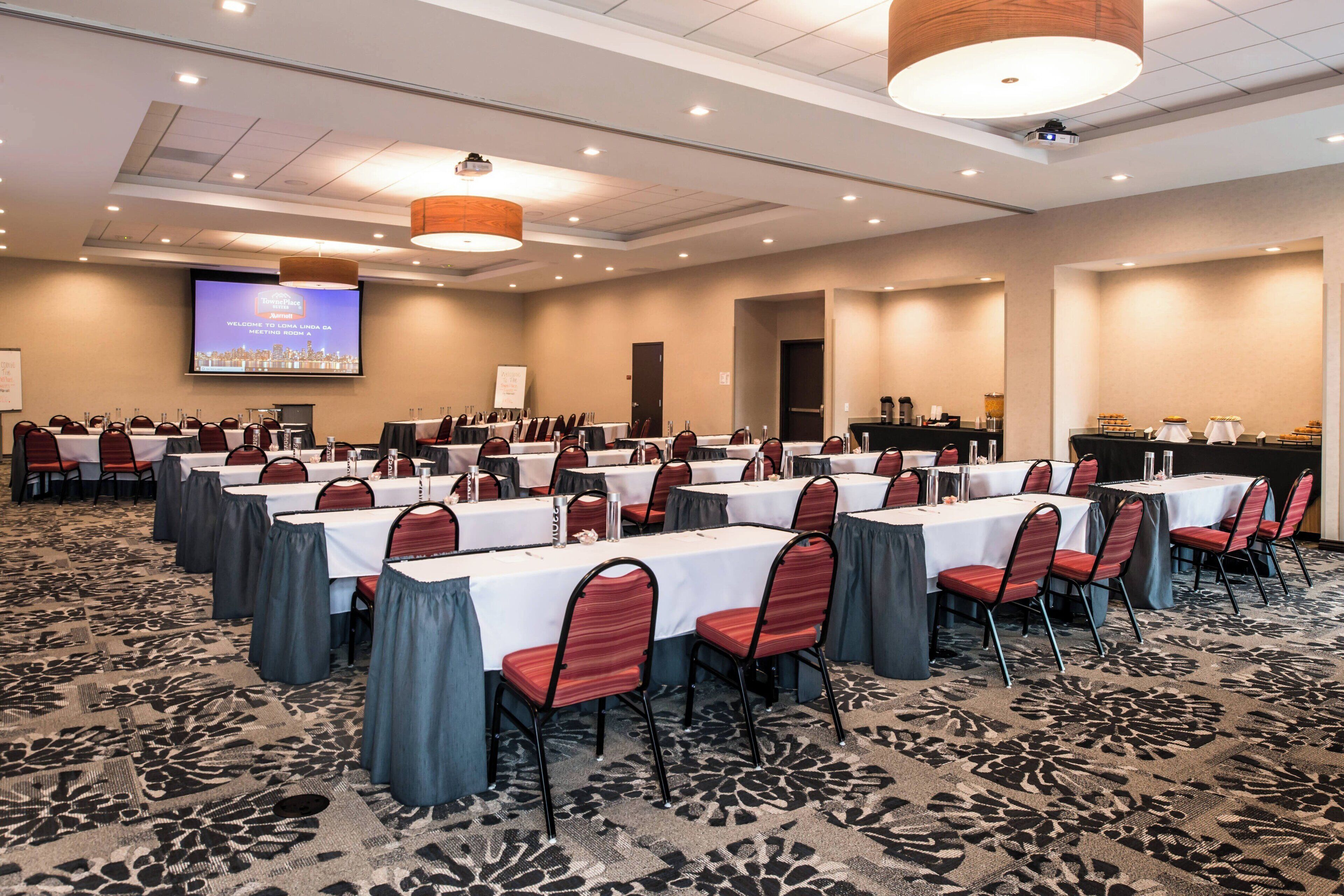 Una sala de conferencias con varias mesas y sillas, una pantalla de proyector y una pizarra.