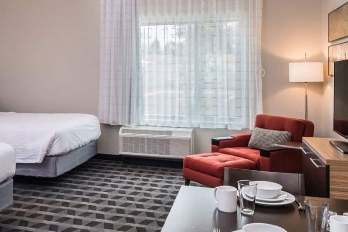 A hotel room with two beds, a red armchair, a dining table with plates and glasses, and a TV.