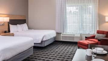 A hotel room with two beds, a red armchair, a dining table with plates and glasses, and a TV.