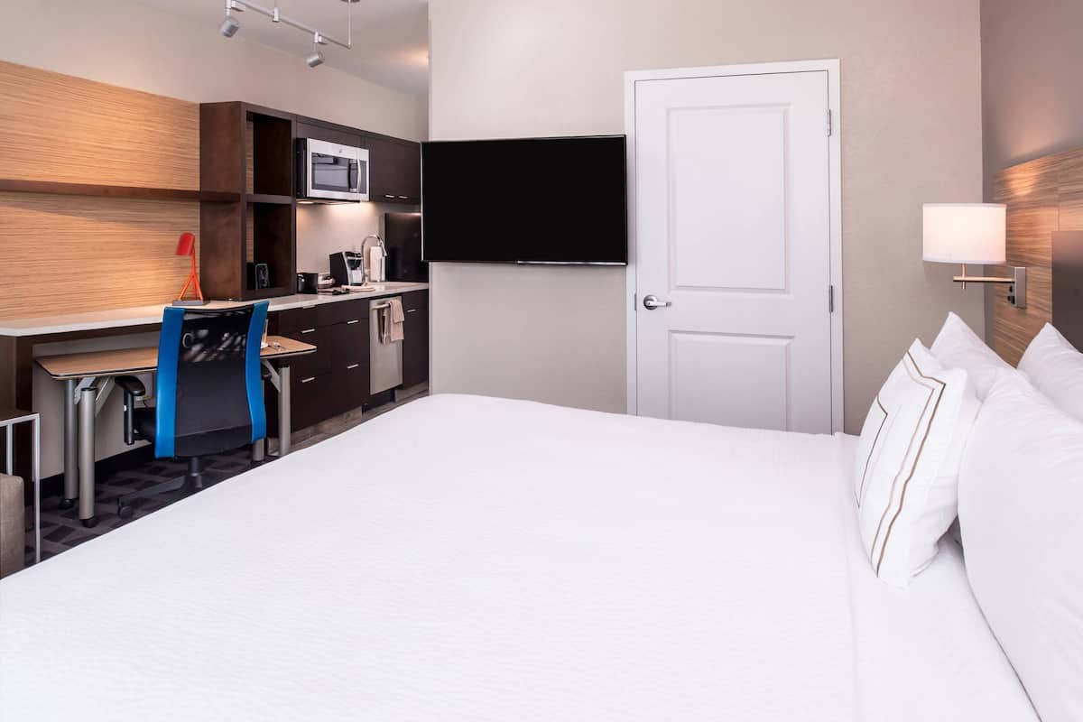 A hotel room with a bed, a desk with a chair, a microwave, a flat-screen TV, and a door.