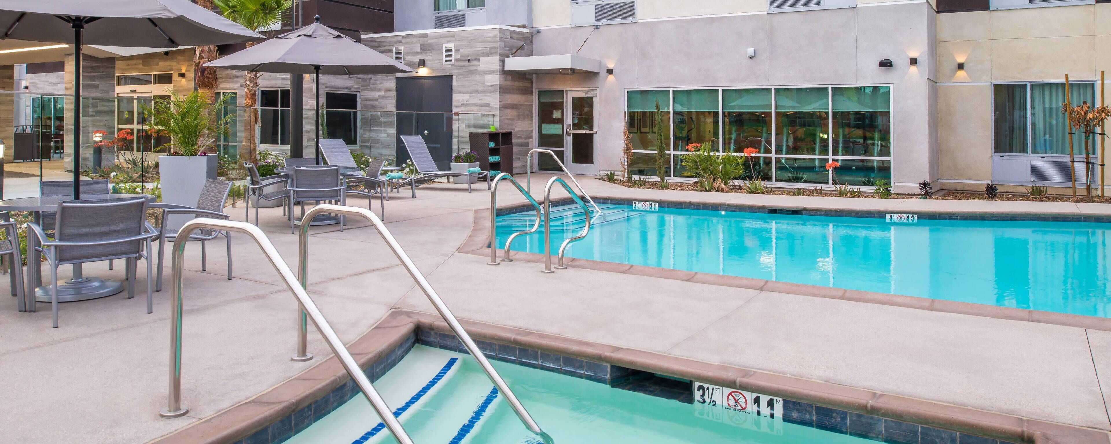 A pool area with lounge chairs, umbrellas, and a clear pool.