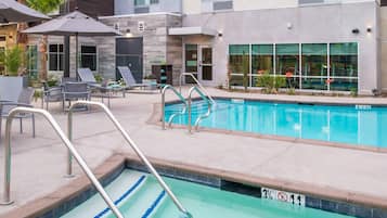 A pool area with lounge chairs, umbrellas, and a clear pool.