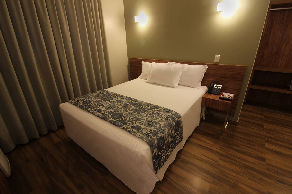 A hotel room with a bed, a nightstand, a telephone, and a wooden floor.