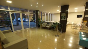 A hotel lobby with a reception desk, seating area, and a glass door entrance. - Ímpar Suítes Barão de Cocais (Barao de Cacais)