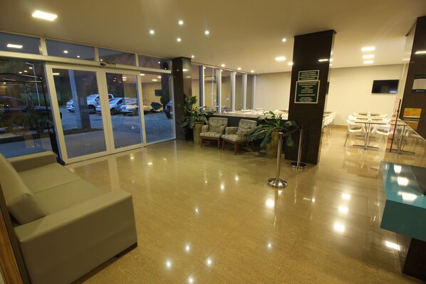 A hotel lobby with a reception desk, seating area, and a glass door entrance. - Ímpar Suítes Barão de Cocais (Barao de Cacais)