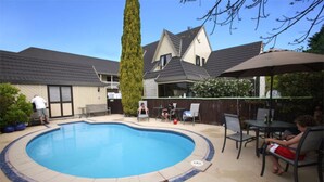 A backyard with a swimming pool, patio furniture, and a tall tree. - Kings Gate Motel (Nelson)