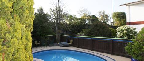 A swimming pool with a tiled deck, surrounded by a wooden fence and greenery.