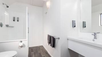 Un baño moderno con ducha, inodoro y lavamanos, con paredes blancas y suelo de madera.