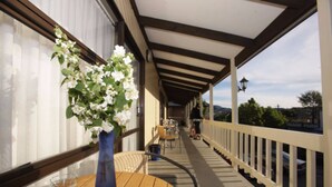 A covered outdoor seating area with a table and chairs, a potted plant, and a view of the street and hills in the background. - Kings Gate Motel (Nelson)