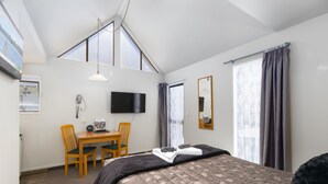 A bedroom with a bed, a desk with a chair, a television, and a window with curtains. - Kings Gate Motel (Nelson)