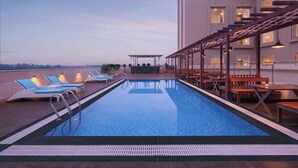 A rooftop pool with lounge chairs and tables, surrounded by a building with multiple windows and a covered seating area. - Fairfield by Marriott Amritsar (Amritsar)
