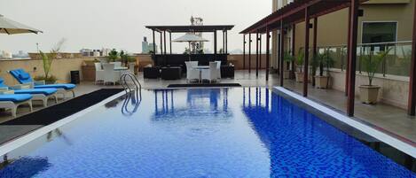 A rooftop swimming pool with lounge chairs and a table, surrounded by potted plants.