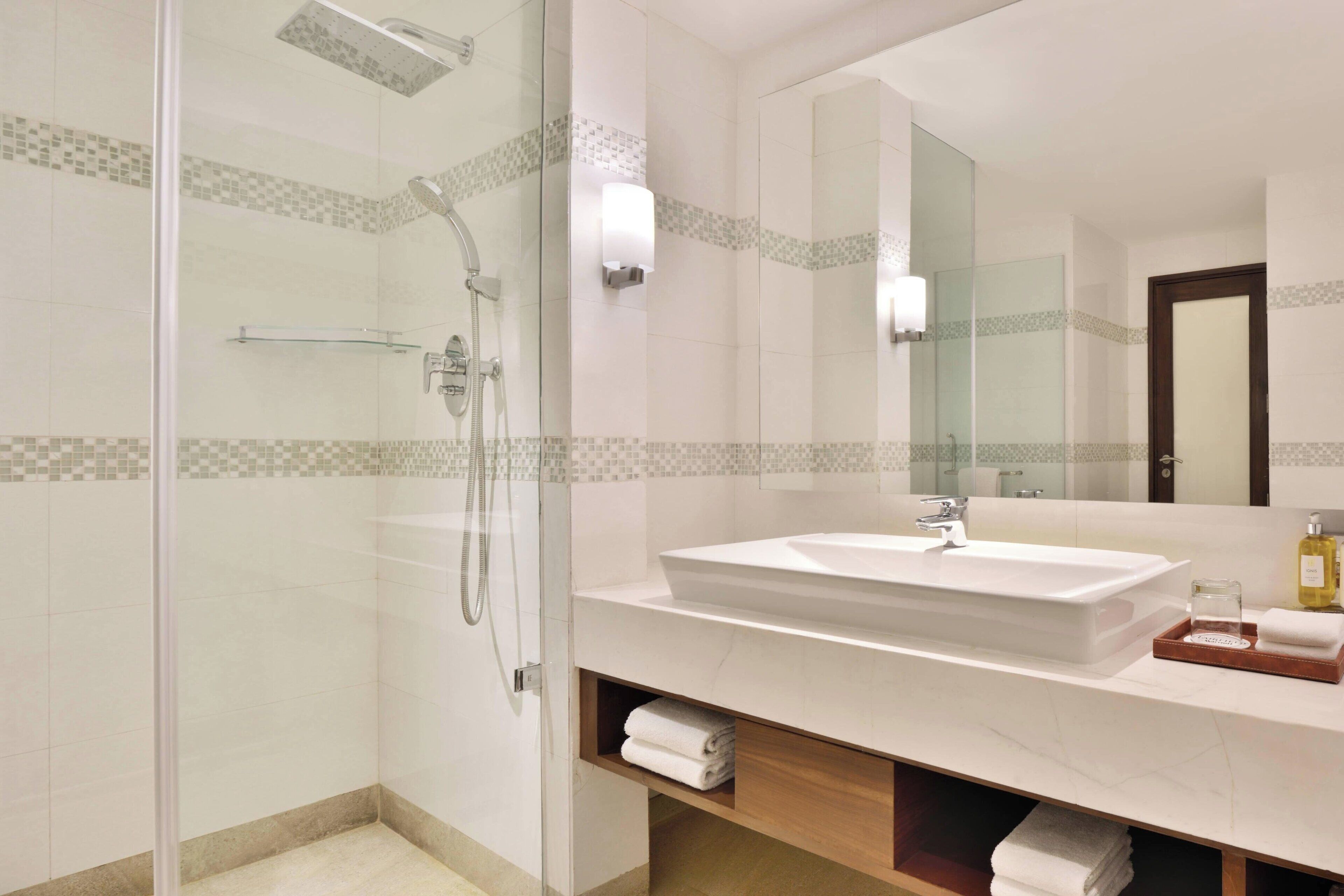 Un baño moderno con ducha de vidrio, un espejo grande y un lavabo blanco con encimera de mármol.