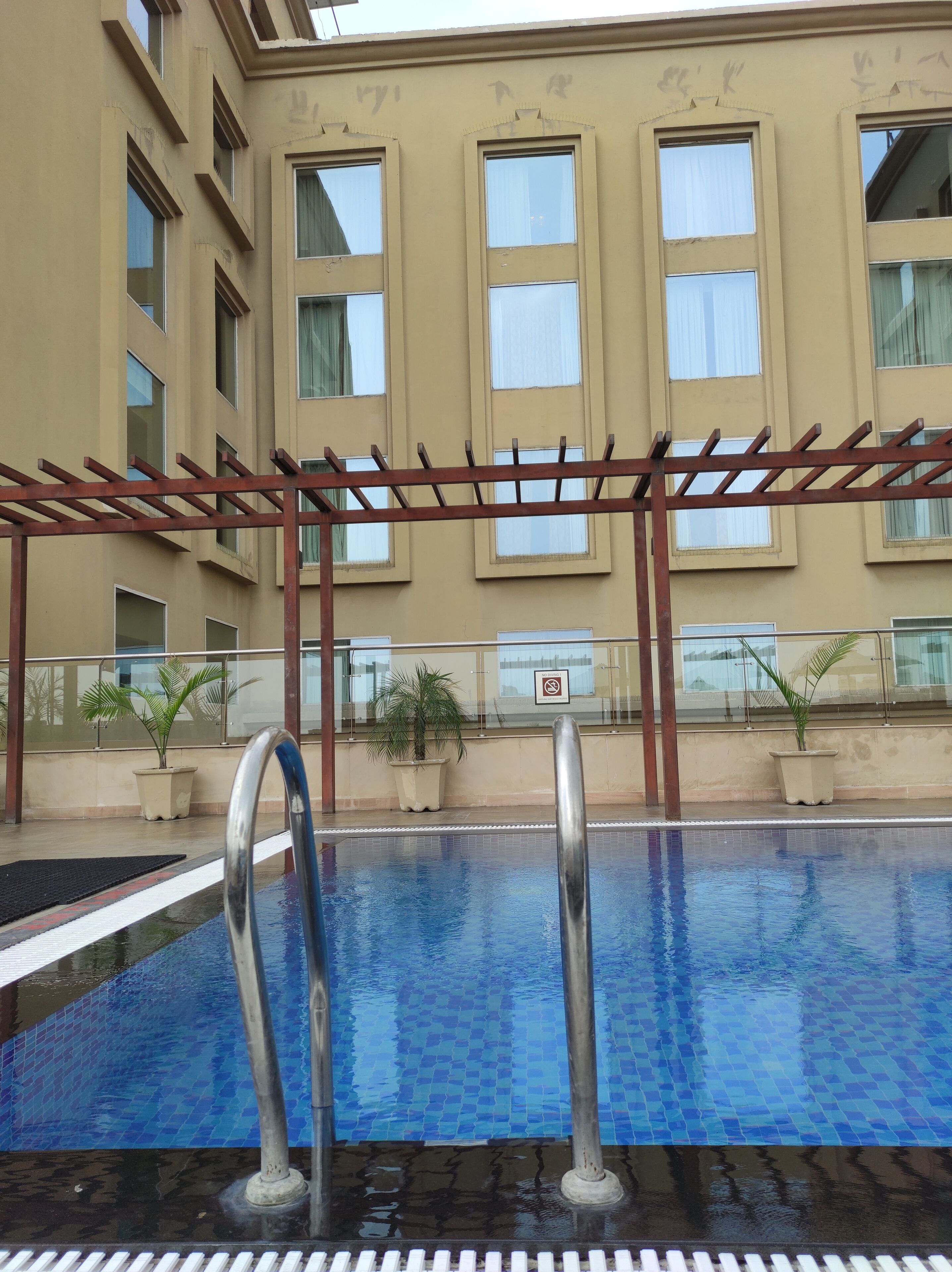 Una piscina con una pergola, piante in vaso e un edificio con ampie finestre sullo sfondo.
