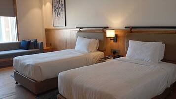 A hotel room with two beds, a sofa, and a bedside table with a lamp.