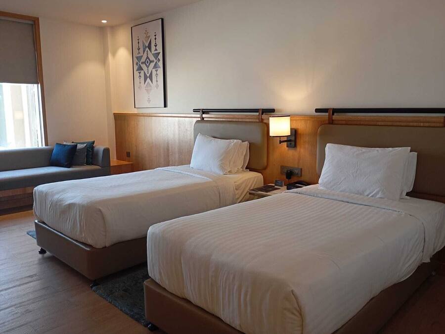 A hotel room with two beds, a sofa, and a bedside table with a lamp.
