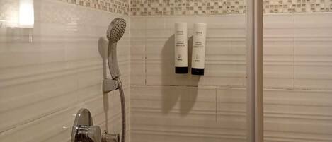 A shower with a handheld showerhead and a wall-mounted showerhead. There are two bottles of shampoo on the wall.