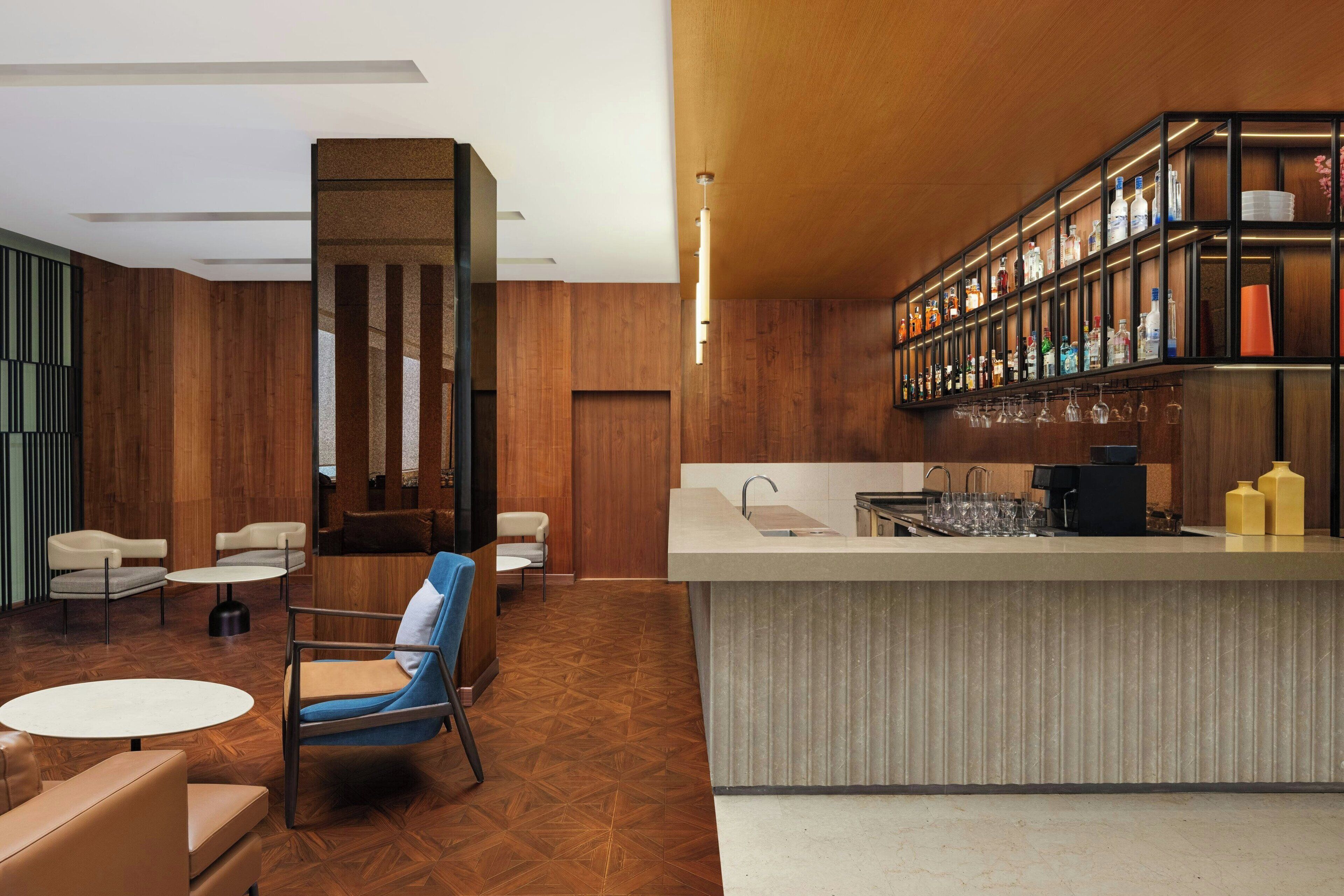 A modern bar area with a wooden floor, seating, and a bar counter with shelves of bottles and glasses.