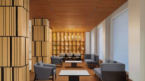 A modern interior with a wooden ceiling, a central seating area with sofas and tables, and a wall of shelves with various items. - Fairfield by Marriott Amritsar (Amritsar)