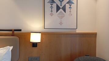 Una habitación de hotel con una cama, una mesita de noche con lámpara, una silla y una obra de arte colgada en la pared.