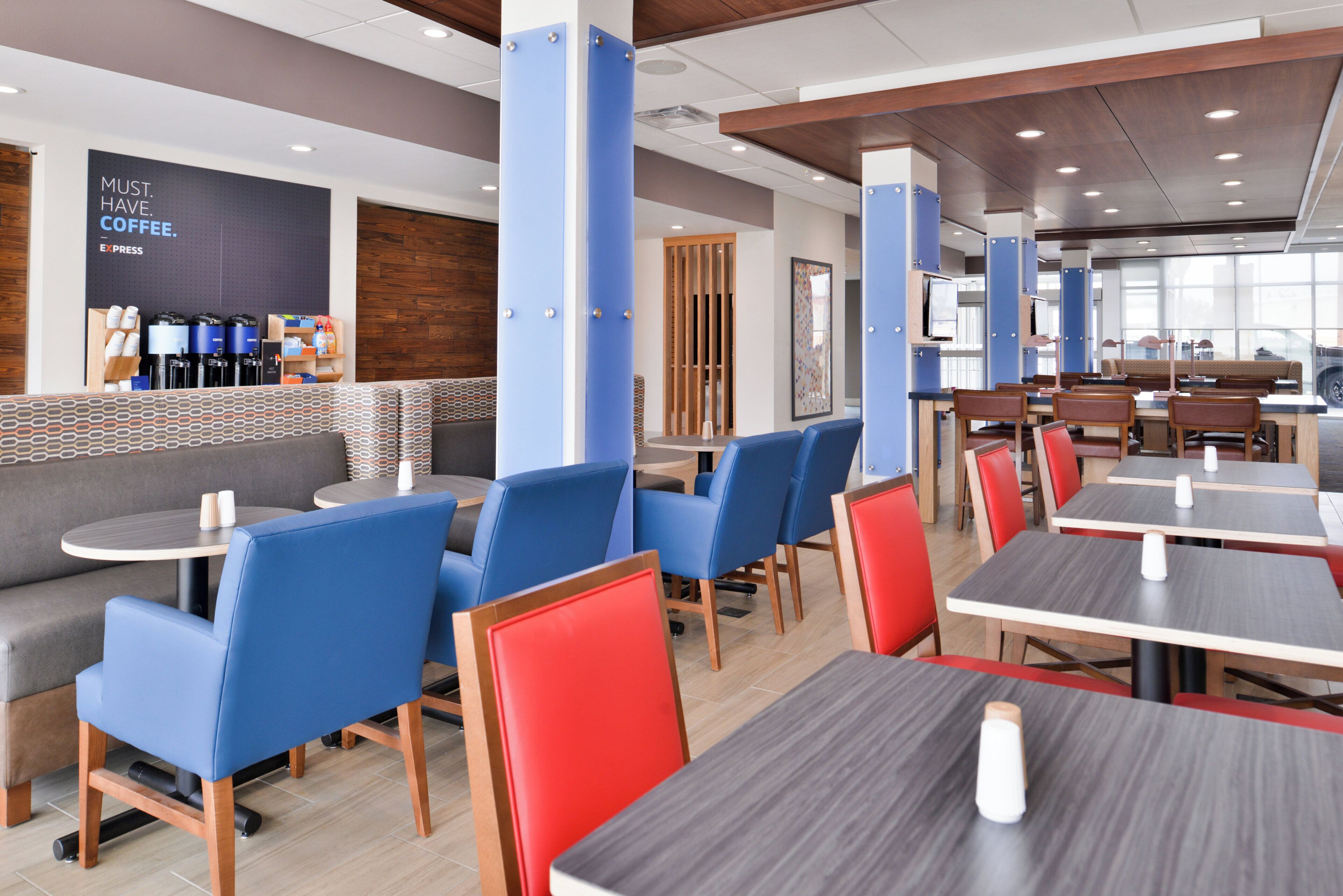 A modern cafe with blue and red seating, a coffee station, and a large window providing natural light.