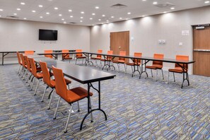 A conference room with a long table, orange chairs, a flat-screen TV on the wall, and a patterned carpet.
