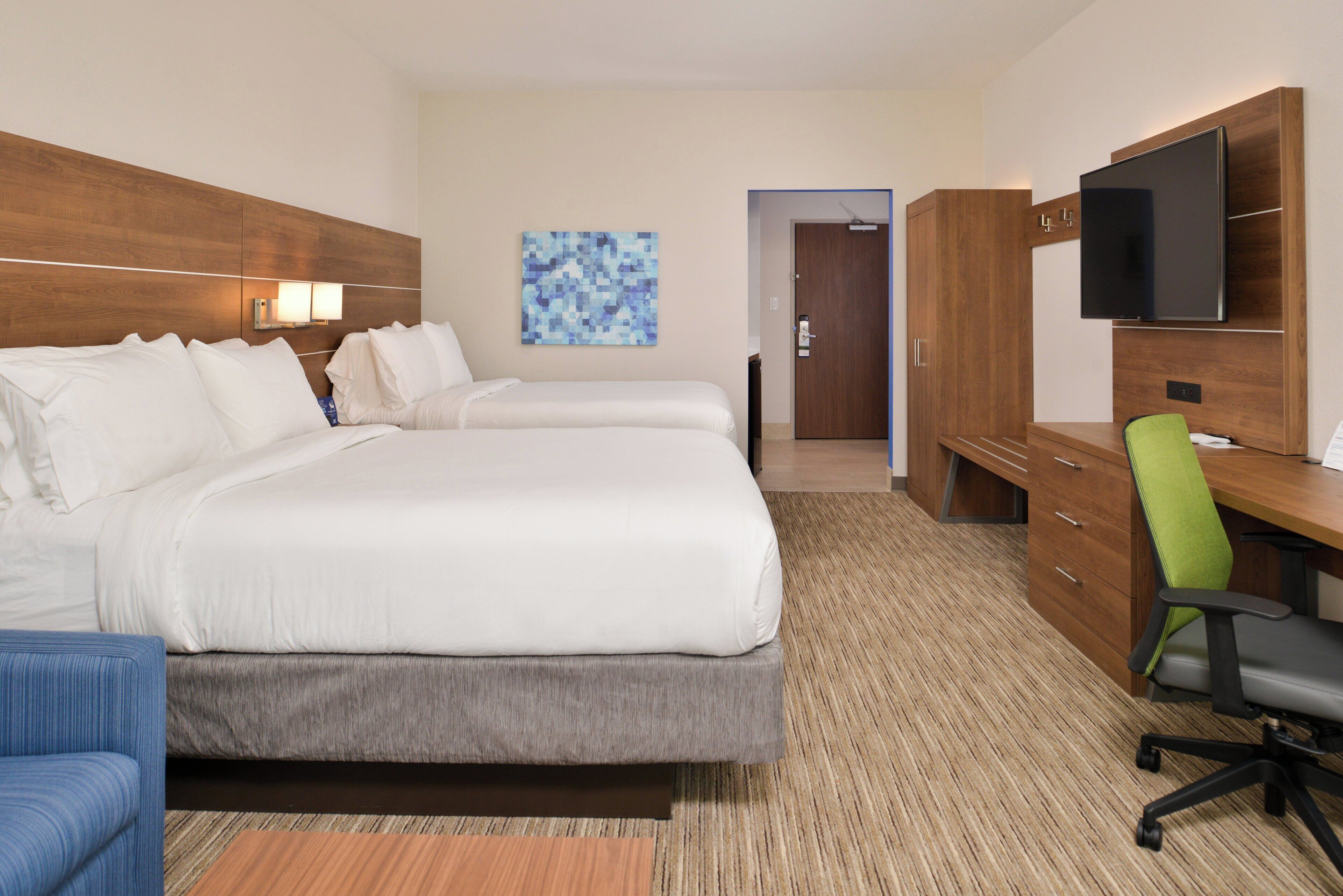 A hotel room with two beds, a desk, a chair, a television, and a door leading to a bathroom.
