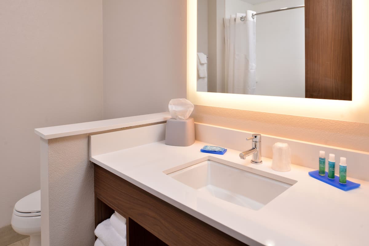 Un baño con lavamanos blanco, un espejo y artículos de aseo.