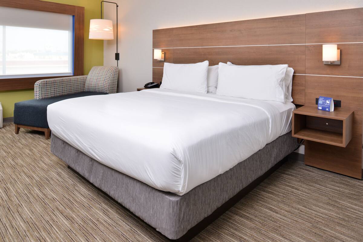 Habitación de hotel con una cama grande, una mesita de noche, una lámpara y vistas al exterior.