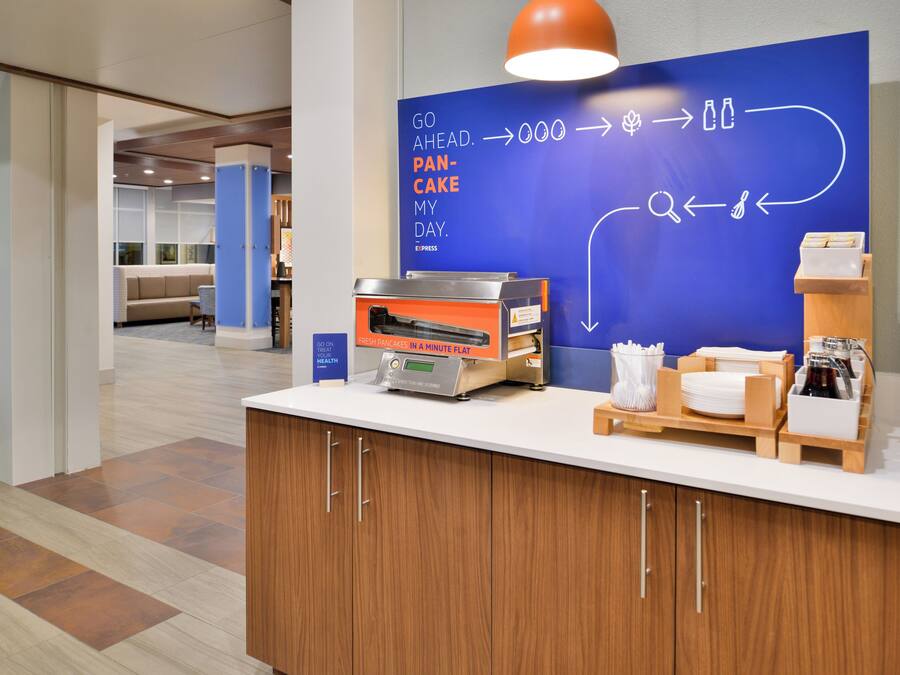 A breakfast station with a digital pancake maker, a coffee machine, and a sign with a health message.