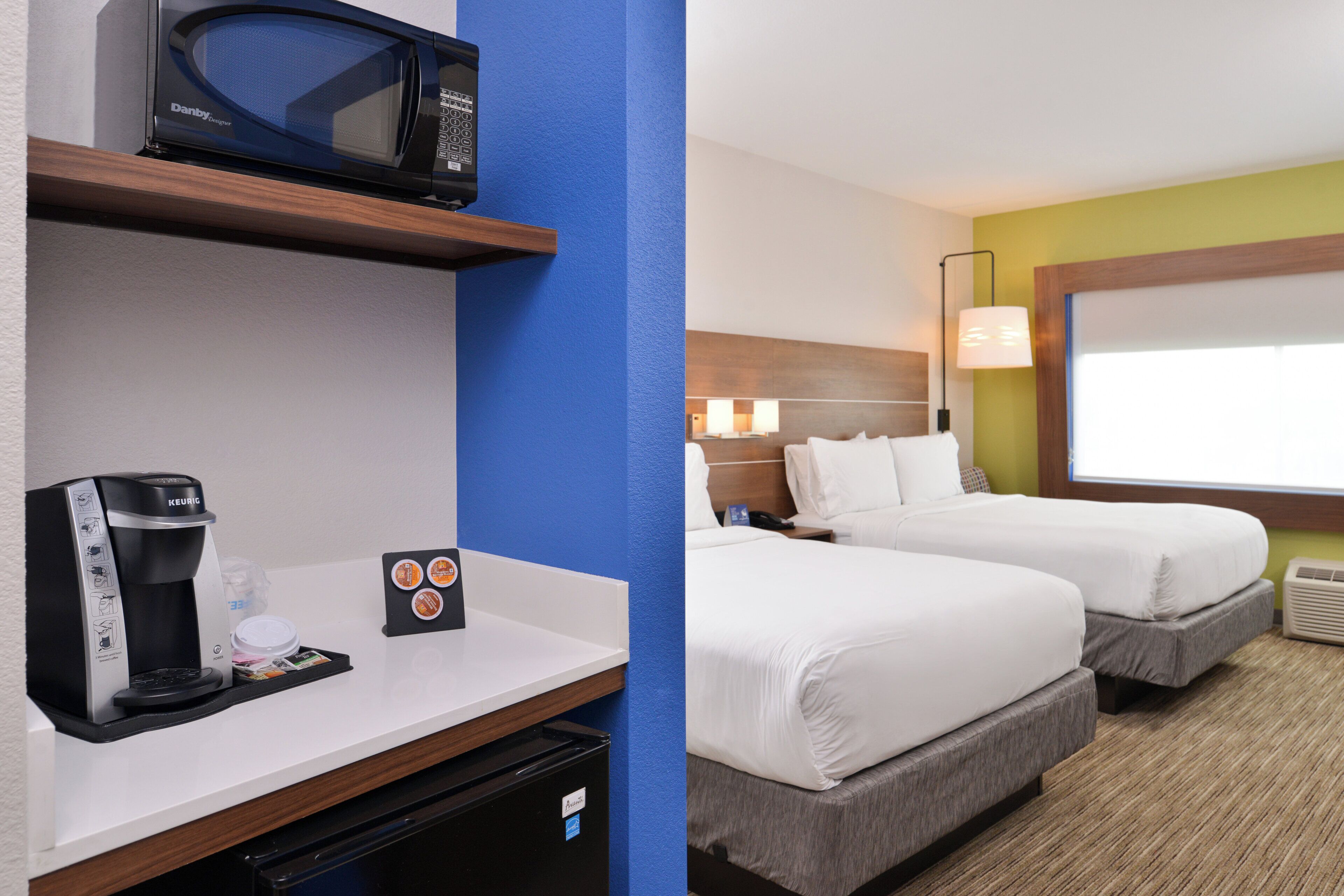 A hotel room with a kitchenette, a microwave, a coffee maker, and two beds.