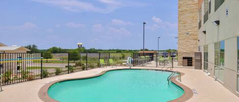 A swimming pool with a curved edge, surrounded by a paved deck and a metal fence.