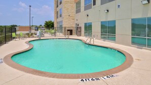 A swimming pool with a brick edge, surrounded by a fence, and adjacent to a building with large windows. - Holiday Inn Express Early by IHG (Early)