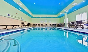 An indoor swimming pool with clear water, surrounded by lounge chairs and tables, and a ceiling with recessed lighting.