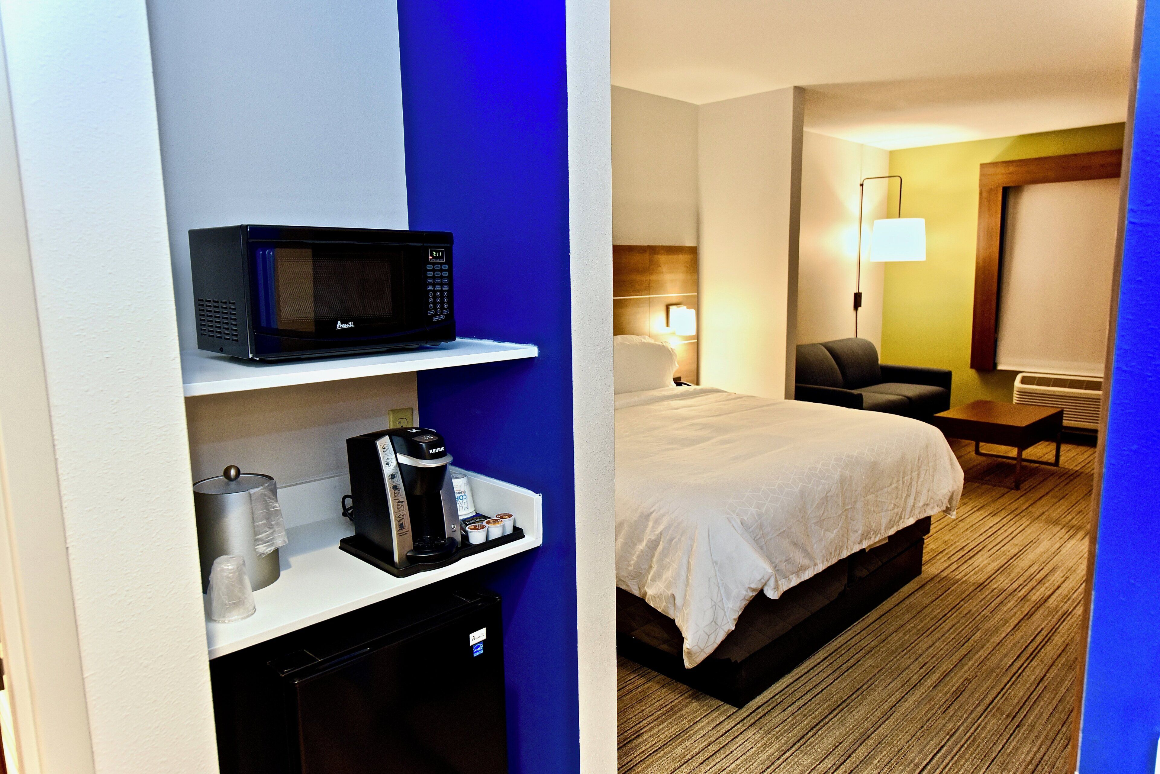 A hotel room with a bed, a desk with a microwave, a coffee maker, and a lamp.
