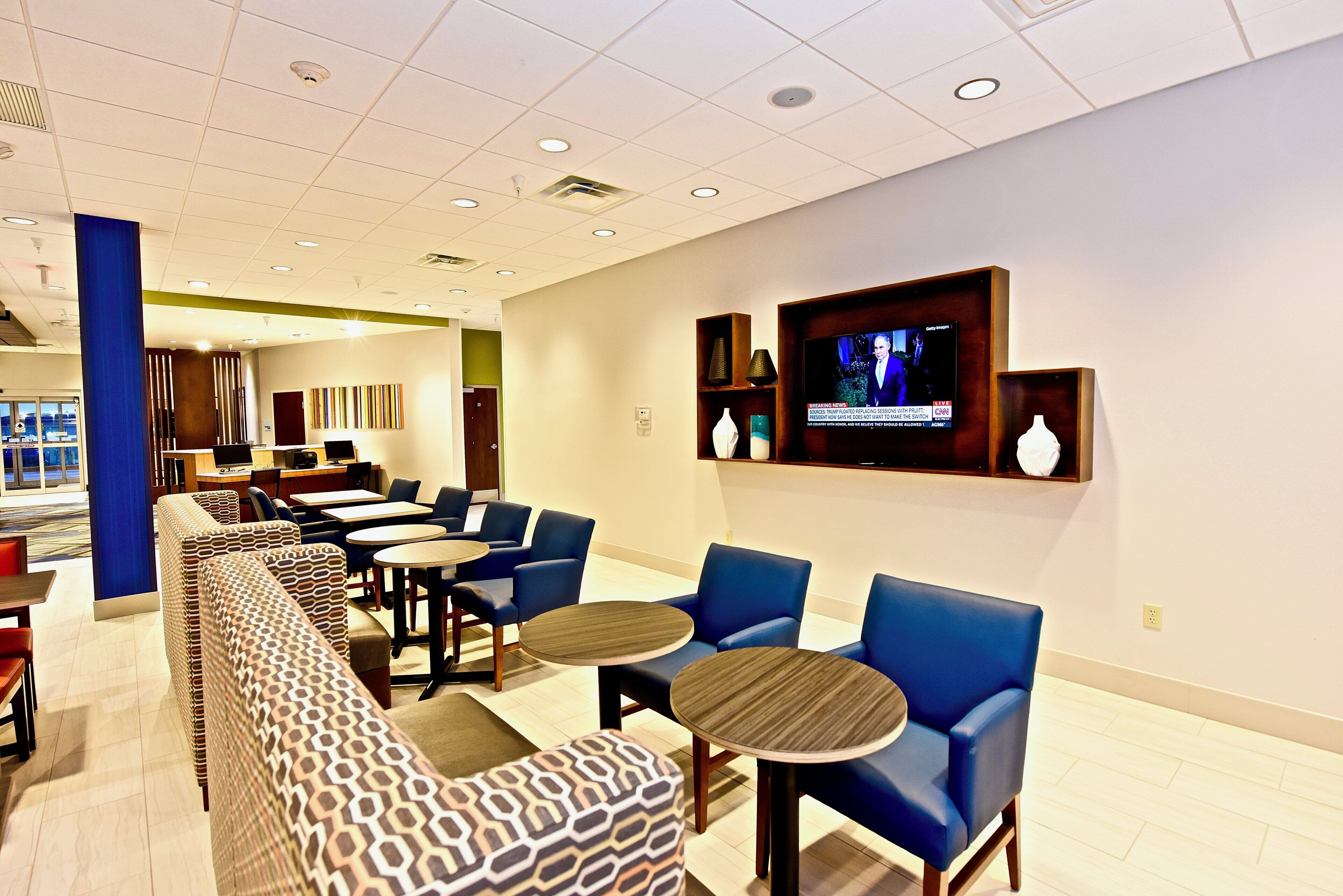 A hotel lobby with seating areas, a television screen, and a reception desk.