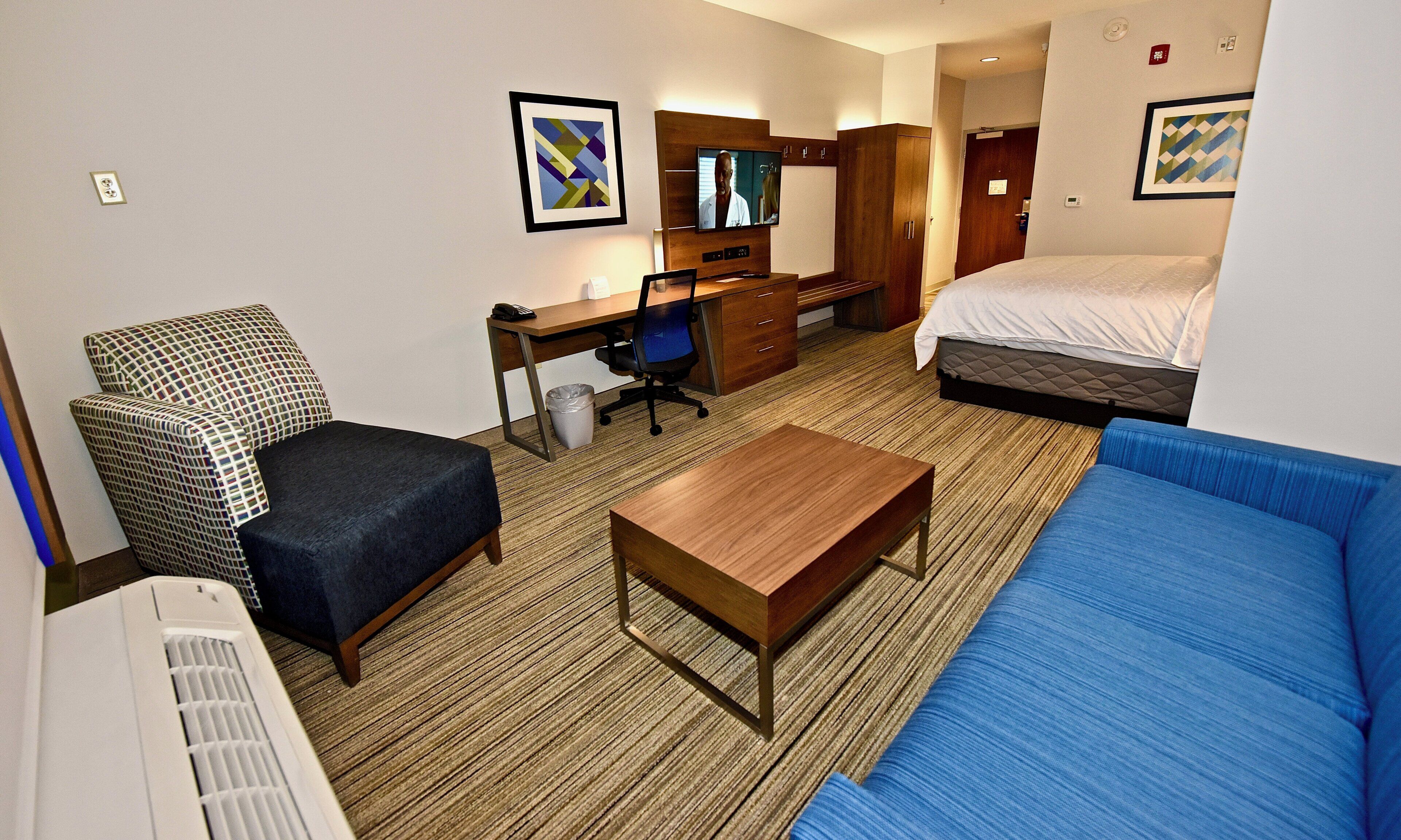 A hotel room with a bed, a desk, a chair, a sofa, and a TV.