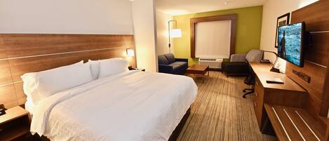 Una habitación de hotel con una cama grande, un escritorio con computadora, una silla, un televisor y una mesita.