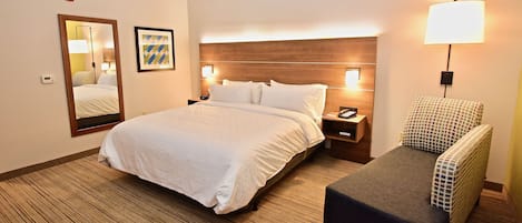 Una habitación de hotel con una cama grande, una mesita de noche, una lámpara, una silla y un espejo.